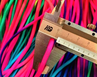 May include: Close-up of a caliper measuring the thickness of a bright pink cord. The cord is surrounded by other cords in various colours, including green, blue, and purple.