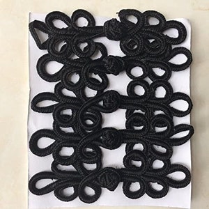 Puede incluir: Cierres de nudo chino negro, también conocidos como cierres de rana, son un elemento decorativo y funcional utilizado en la ropa tradicional china. Estos nudos están hechos de cordón trenzado y se utilizan a menudo para abrochar prendas o agregar un toque decorativo.