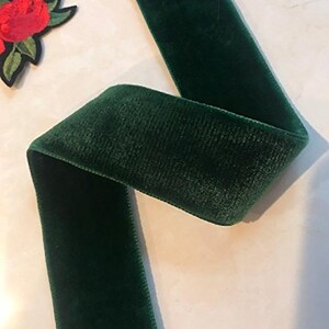 Puede incluir: Un rollo de cinta de terciopelo verde oscuro. La cinta es suave y aterciopelada, con un brillo sutil.