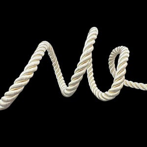 May include: A close-up of a white rope cord, twisted and looped into a decorative shape against a black background.