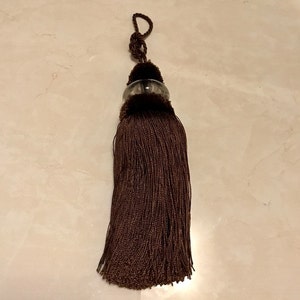 May include: A brown tassel with a clear glass bead at the top. The tassel is made of a soft, silky material and is approximately 10 inches long.