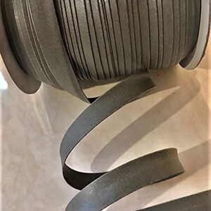 May include: A spool of gray leather cord, wound tightly and ready to be used for crafting projects. The cord is smooth and has a subtle sheen.