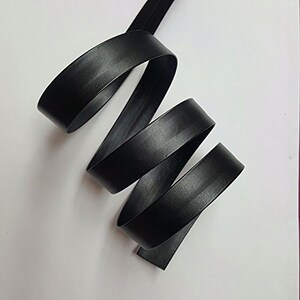 May include: Black leather ribbon, folded and coiled, showing the smooth texture and the edges of the ribbon.