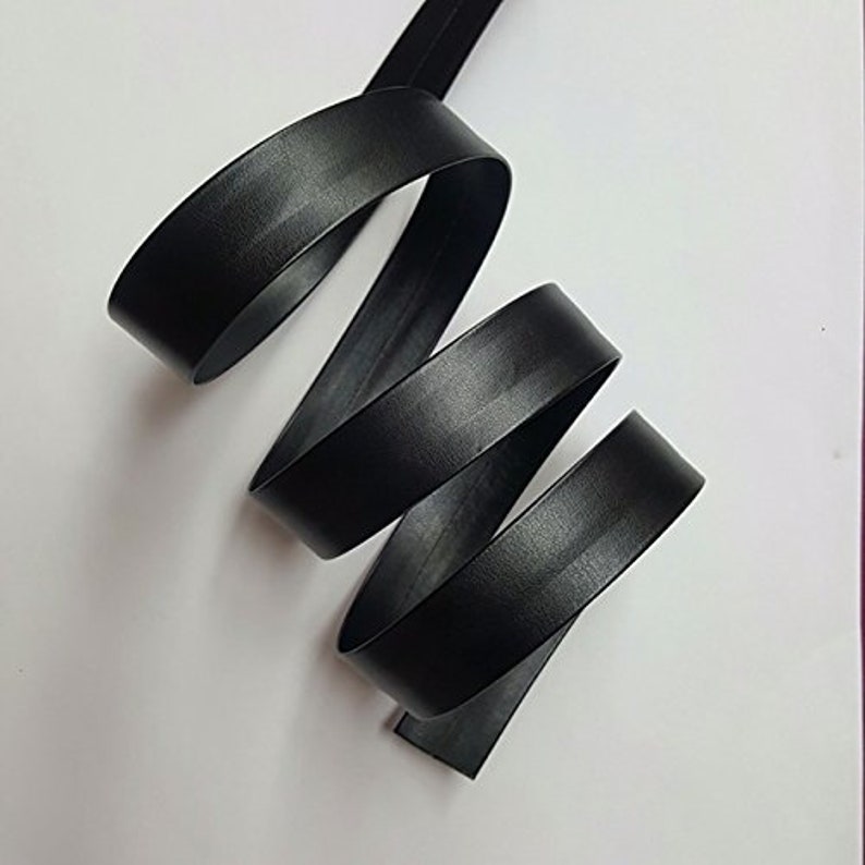May include: Black leather ribbon, folded and coiled, showing the smooth texture and the edges of the ribbon.