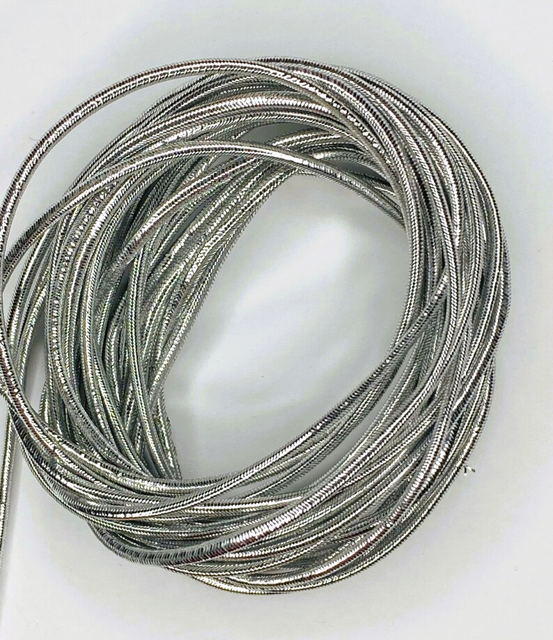 May include: A coil of silver metallic cord, perfect for crafting jewelry or adding a touch of sparkle to projects.