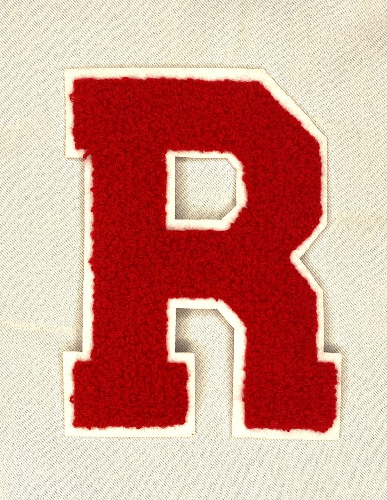 May include: A red, varsity-style letter "R" patch with a white border. The letter has a textured, fuzzy appearance and is set against a light-colored fabric background. This patch is suitable for jackets, bags, or other apparel.