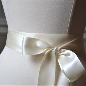 May include: A white satin ribbon tied in a bow around a dress form. The ribbon is approximately 5 cm wide.