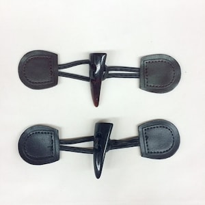 May include: Two sets of brown and black leather toggles with horn-like toggles. The toggles are connected by a brown cord.