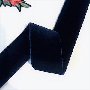 Puede incluir: Un rollo de cinta de terciopelo azul oscuro. La cinta est&aacute; doblada por la mitad y los bordes son visibles.