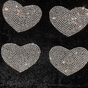 Puede incluir: Cuatro parches en forma de corazón de diamantes de imitación plateados sobre un fondo negro.