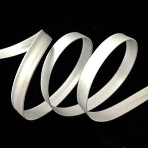 May include: White satin ribbon with a double-fold edge. The ribbon is curled and twisted, showing the smooth, shiny surface.
