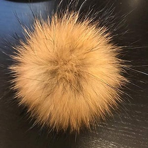 May include: A fluffy, light brown faux fur pom pom. The pom pom is soft and fluffy, and would be perfect for adding a touch of whimsy to a hat or scarf.