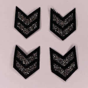 Può includere: Quattro toppe in feltro nero con un design a doppio chevron. Ogni chevron è ricoperto di glitter argentato.