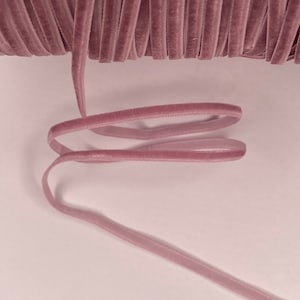 May include: A spool of dusty rose velvet ribbon. The ribbon is thin and has a smooth, silky texture.