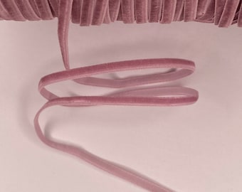 Puede incluir: Una bobina de cinta de terciopelo rosa polvoriento. La cinta es fina y tiene una textura suave y sedosa.