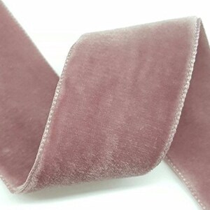 Puede incluir: Un rollo de cinta de terciopelo rosa polvoriento. La cinta es suave y tiene un brillo sutil.