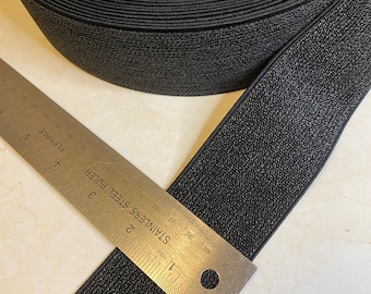 May include: A roll of black elastic with a textured surface. The elastic is measured with a ruler, showing it is 1 inch wide.