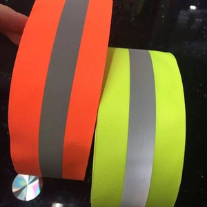 May include: Two rolls of reflective tape, one orange and one yellow, with a silver reflective strip in the center.