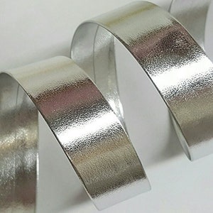 May include: Silver metallic ribbon with a textured surface. The ribbon is rolled up and appears to be shiny.