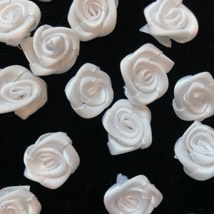 May include: A collection of white satin ribbon roses. The roses are small and delicate, and they are perfect for adding a touch of elegance to any craft project.