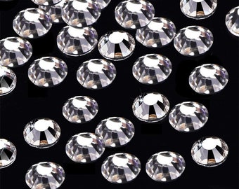 Puede incluir: Una dispersión de piedras de cristal redondas transparentes sobre un fondo negro. Las piedras de cristal son de varios tamaños y tienen una superficie facetada y reflectante.