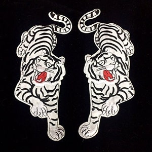May include: Two white embroidered iron-on patches of tigers with black stripes and red mouths. The tigers are facing opposite directions.