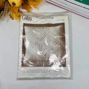 Puede incluir: Un kit de almohada empaquetado de la marca "Cathy Candlewickery". El kit presenta una almohada blanca con un diseño serigrafiado de uvas y hojas. La almohada mide 45,7 x 45,7 cm.