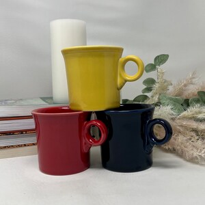 Puede incluir: Tres tazas de cerámica apiladas una encima de la otra. La taza de arriba es amarilla, la taza del medio es roja y la taza de abajo es azul.