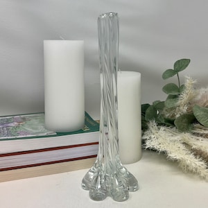 May include: A clear glass vase with a twisted design and a wide base. The vase is sitting on a stack of books and a white surface.