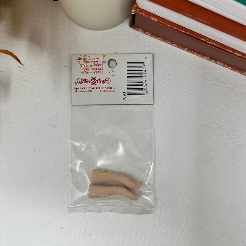 May include: A package of Fibre-Craft doll hands. The package includes two tan-colored hands with gold-colored accents. The packaging has a label with the Fibre-Craft logo and the text "Can be used with the following wings: Brass #3431, Papier #3434, Nylon #3438."