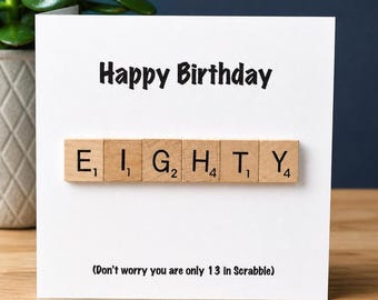 May include: A white greeting card with the black text Happy Birthday at the top. The center features six wooden letter tiles spelling EIGHTY with numerical values. Below, the text reads Don't worry you are only 13 in Scrabble.