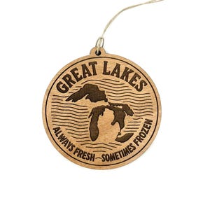 May include: A round wooden ornament with the words "Great Lakes" and the phrase "Always Fresh - Sometimes Frozen" engraved around a map of the Great Lakes. A twine loop is attached for hanging.