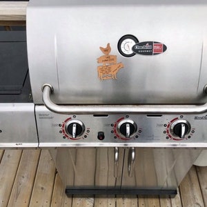 May include: A stainless steel Char-Broil TRU Infrared gas grill with four burners and a side burner. The grill has a black lid with a thermometer and a Char-Broil TRU Infrared Gourmet logo.