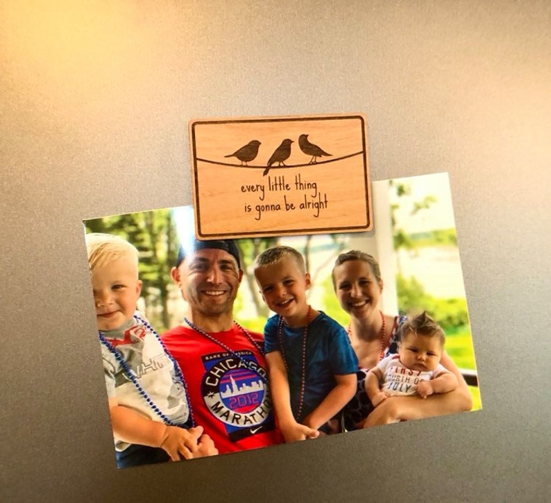 Puede incluir: Un letrero de madera con tres p&aacute;jaros posados en un alambre. El letrero dice "every little thing is gonna be alright". Una foto de una familia con dos ni&ntilde;os peque&ntilde;os y una ni&ntilde;a beb&eacute; est&aacute; pegada al letrero con un im&aacute;n.