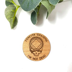 May include: Wooden coin with a Grateful Dead skull and the text "Forever Grateful I'm Not Dead" and a symbol of a square inside a circle.