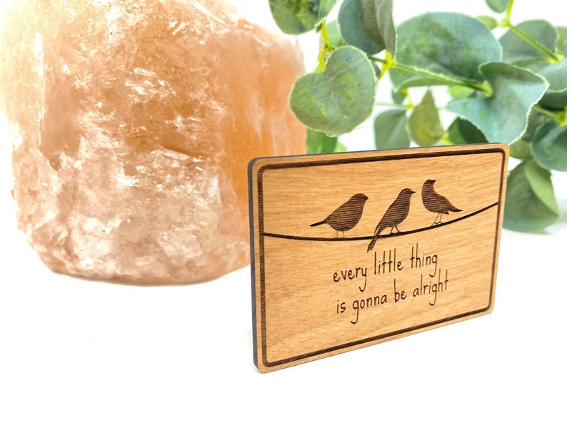 Puede incluir: Un letrero de madera con veta de madera marr&oacute;n claro y borde marr&oacute;n oscuro. Tres p&aacute;jaros est&aacute;n posados en un alambre con el texto "every little thing is gonna be alright".