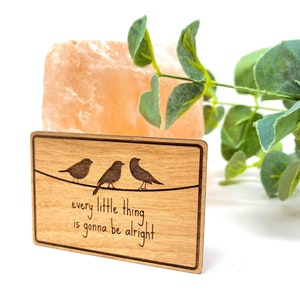 Puede incluir: Un letrero de madera con un acabado de madera de grano marr&oacute;n claro. El letrero presenta tres p&aacute;jaros posados ​​en un alambre con el texto "every little thing is gonna be alright".