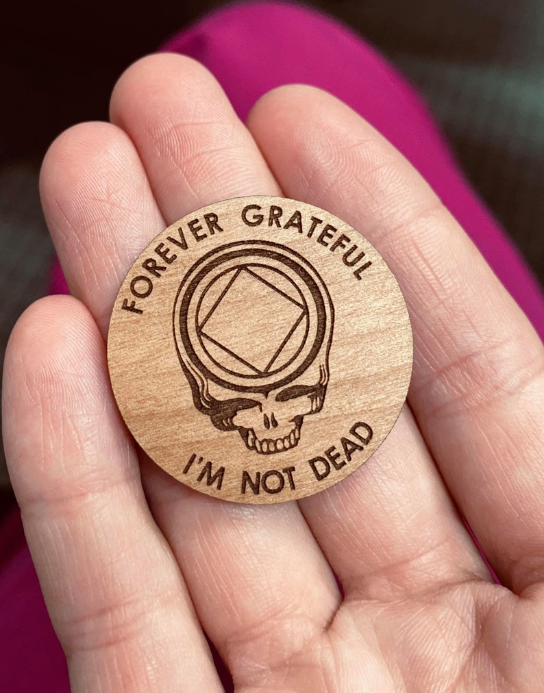 May include: A wooden token with a Grateful Dead skull and the text "Forever Grateful I'm Not Dead" and a square inside a circle.