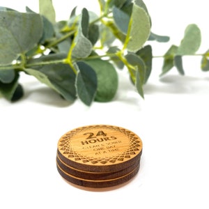 Puede incluir: Un posavasos redondo de madera con el texto "24 HOURS CLEAN & SOBER ONE DAY AT A TIME" grabado en &eacute;l. El posavasos tiene un patr&oacute;n decorativo alrededor del borde.