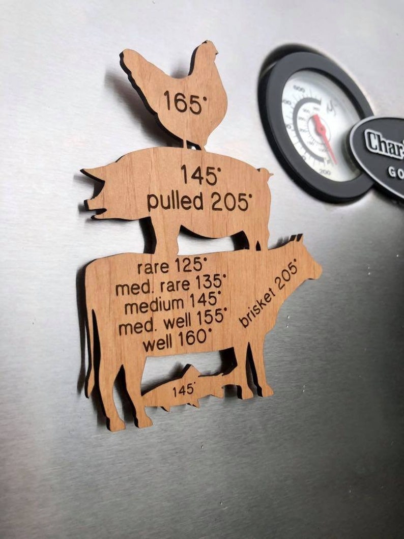 May include: Wooden cutouts of a chicken, pig, cow, and fish with internal temperature guidelines for cooking. The chicken cutout has a temperature of 165 degrees Fahrenheit. The pig cutout has a temperature of 145 degrees Fahrenheit and a pulled temperature of 205 degrees Fahrenheit. The cow cutout has a temperature range of 125 to 160 degrees Fahrenheit for different levels of doneness. The fish cutout has a temperature of 145 degrees Fahrenheit. The cow cutout also has the text "brisket 205" written on it.