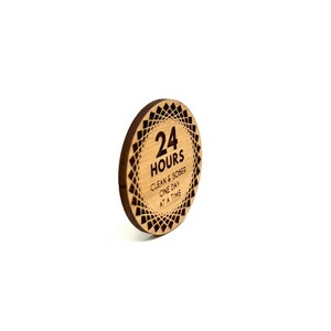 Puede incluir: Un token redondo de madera con un dise&ntilde;o geom&eacute;trico en blanco y negro. El token tiene el texto "24 HOURS" y "CLEAN & SOBER ONE DAY AT A TIME" grabado en &eacute;l.