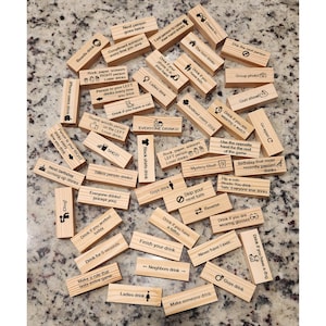 May include: A collection of wooden blocks with various drinking game instructions printed on them. The blocks are scattered on a speckled surface. Text includes phrases like "Drink if you have a dog" and "Everyone drinks!"