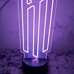 May include: A purple LED night light shaped like the letter "M" with a black base and an on/off switch.
