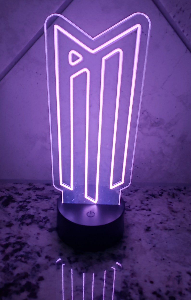 May include: A purple LED night light shaped like the letter "M" with a black base and an on/off switch.