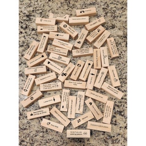 May include: A collection of wooden blocks with various drinking game instructions printed in black. Instructions include "Drink if you have a tattoo," "Everyone drinks," and "Next person goes TWICE!" The blocks are scattered on a speckled surface.