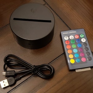 May include: A black circular base with a light strip on top, a black USB cable, and a remote control with a variety of colored buttons labeled "Magic Lighting Remote Controller".