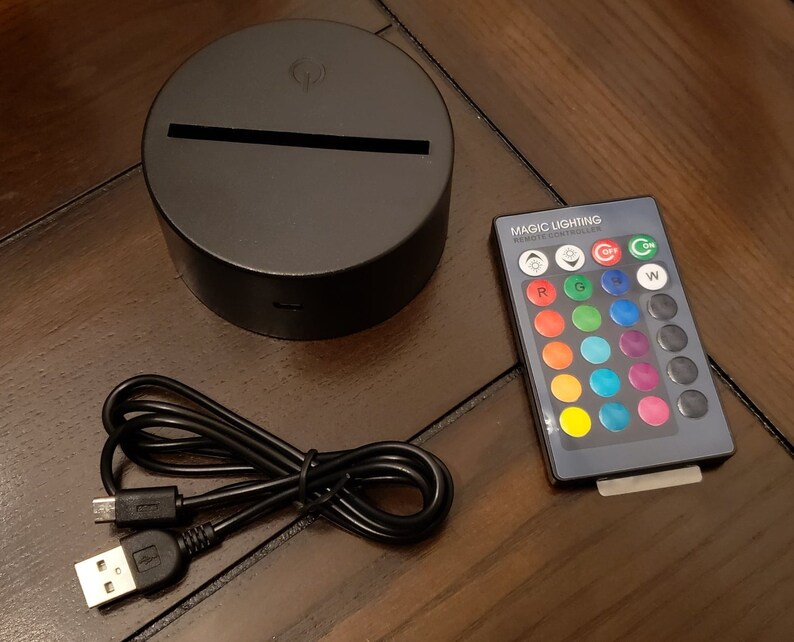 May include: A black circular base with a light strip on top, a black USB cable, and a remote control with a variety of colored buttons labeled "Magic Lighting Remote Controller".