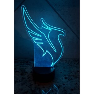 May include: A blue LED night light shaped like a bird with wings spread out. The light is on a black base.