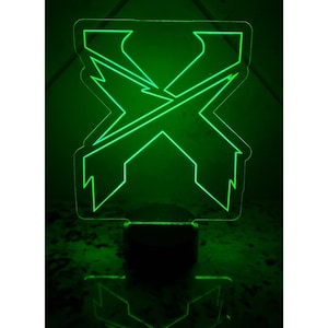 May include: A green acrylic night light shaped like the letter X. The light is on and illuminating the surrounding area.