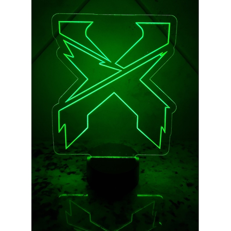 May include: A green acrylic night light shaped like the letter X. The light is on and illuminating the surrounding area.
